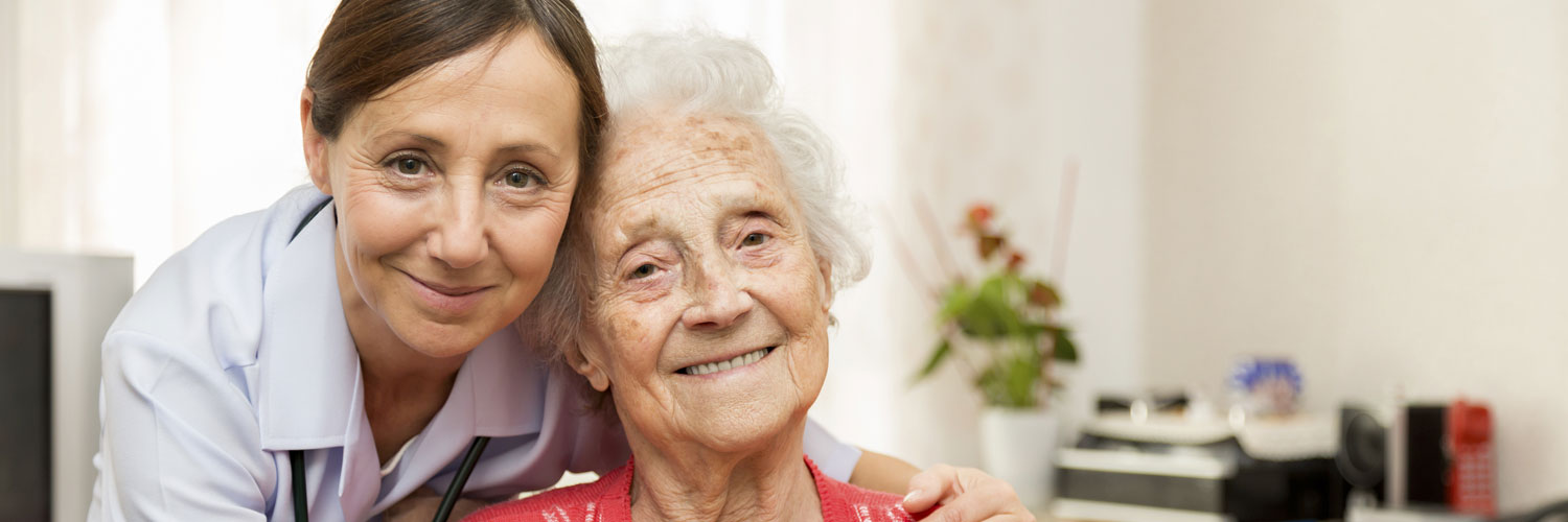 Caregiver and elderly woman smiling at the camera
